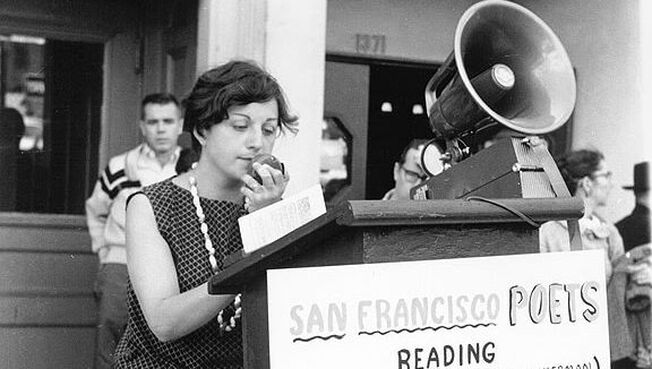 Picture ruth weiss in the 1950s speaking in public with a loud projector 